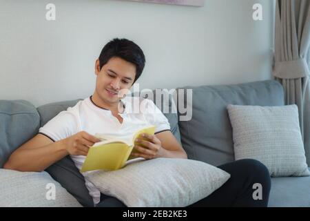Asian man are sitting reading books, resting on the sofa in the living room in the house. Stock Photo