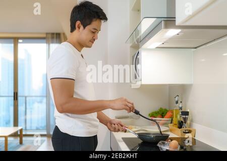 Asian man are cooking American breakfast by frying a fried egg in  pan in their kitchen at home. Stock Photo