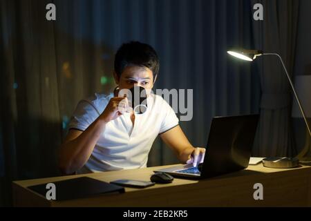 Asian man are drinking tea or coffee while working in late night to relieve drowsiness and make it possible to have a strong to work again. Stock Photo