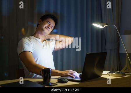 Asian man are stretch lazily while working long hours in front of a computer in late night in living room at home. Stock Photo