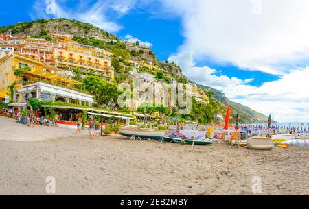 Tourists enjoy the sandy beach, restaurants, resorts and promenade at the coastal hillside city of Positano, Italy on the Amalfi Coast. Stock Photo