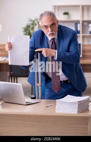 Old male employee after accident working in the office Stock Photo