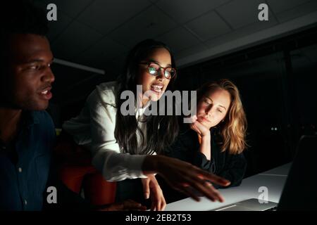 Young female businesswoman discussing the project with her two colleagues in dark office till late night Stock Photo