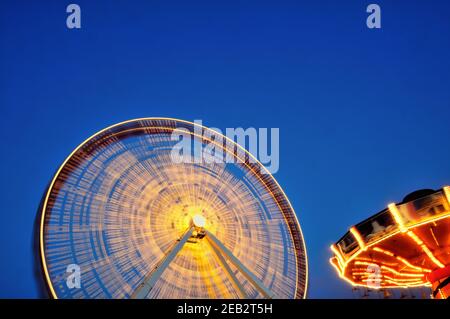 Chicago, Illinois, USA. The Ferris wheel at Navy Pier in Chicago is a blur as it makes its slow circular journey along with a carousel ride. Stock Photo