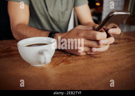 Closeup of male hands holding phone with coffee mug on side while sitting in cafe Stock Photo