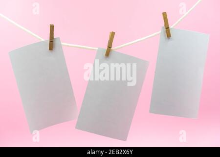 Multiple empty paper sheet for notes that hang on a rope with clothespins and isolated on pink. Blank white photo hanging on rope concept Stock Photo