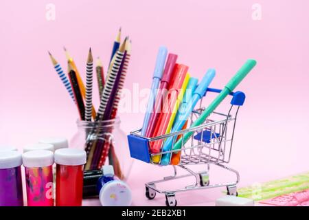 Bright stationery objects in mini supermarket cart on pink background. Back to school concept. Stock Photo