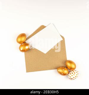 Easter festive decoration. Top view of easter eggs colored with golden paint and empty mock-up card in a kraft envelope. Various dotted designs. White Stock Photo