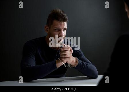 Suspect or criminal man with handcuffs being interviewed by detectives in dark interrogation room Stock Photo