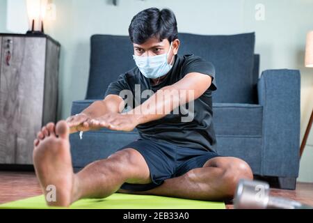 Young man with face mask busy in work out or doing stretching exercise at home - concept of new normal, home gym due to coronavirus covid-19 outbreak. Stock Photo