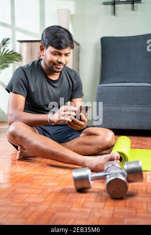 Young man busy using mobile phone during work out - Millennial checking online exercise tutorials for workout - concept of home gym due to coronavirus Stock Photo