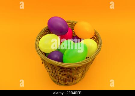 Wicker basket with colorful Easter eggs on yellow paper background. Stock Photo