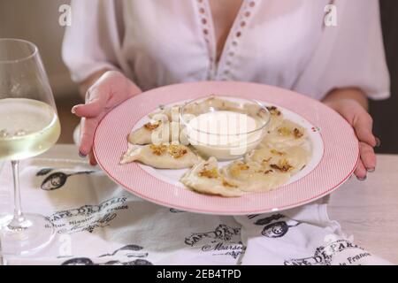 Female hands hold a plate with dumplings and sour cream Stock Photo