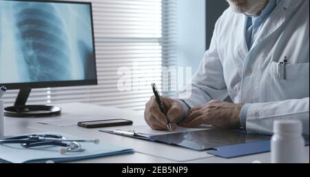 Professional doctor sitting at desk and writing a medical prescription for a patient Stock Photo
