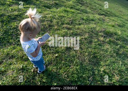 Cute caucasian blond girl playing or learning at mobile phone with black screen Stock Photo