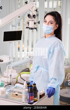Beautiful female doctor in medical safety suit standing in stomatology cabinet. Woman wearing protective face mask and sterile gloves. Concept of dentistry, stomatology and healthcare. Stock Photo