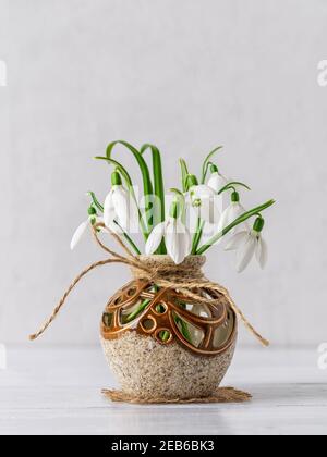 White delicate snowdrops in a round brown ceramic vase against a light gray background. Small beautiful bouquet of the first spring flowers Galanthus Stock Photo