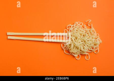 Chopsticks with cooked noodles on orange background Stock Photo