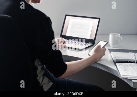 Man using phone and laptop in home office. Online college application, digital insurance, loan or mortgage document. Internet research with technology. Stock Photo