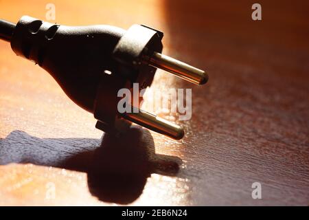 Black power plug on a brown wooden table. Side view, closeup Stock Photo