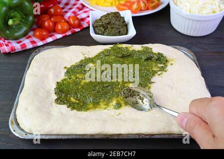 Hand spreading pesto sauce on the pizza dough before baking Stock Photo
