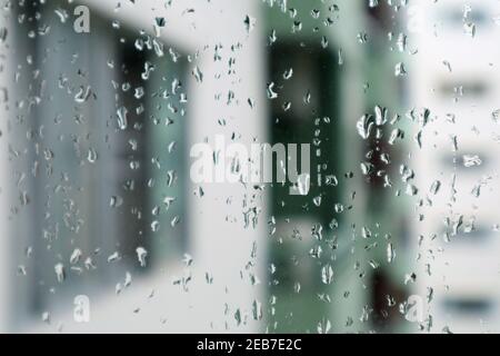 Closeup the rain drops on window's glass with blurry modern buildings in background Stock Photo