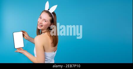 Banner,long format. Cute girl in rabbit ears, holding a tablet with a blank white screen in her hands. Smiling and posing for the camera. Women's blog Stock Photo