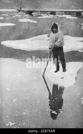 An early 20th century photo of a Labrador Inuit boy clad in a traditional seal skin parka punting on an ice floe circa 1912 Stock Photo