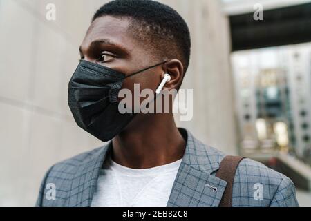 Confident african american man posing in face mask and earphones outdoors Stock Photo