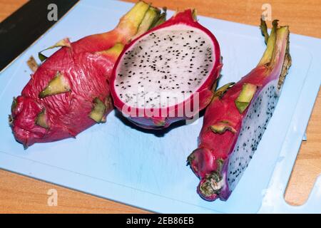white pitahaya; sliced on a blue plastic cutting board. half; quarter; pieces of tropical exotic fruit with bright pink peel and gray pulp with small Stock Photo