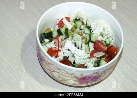 vegetable salad with fresh chopped tomatoes, cucumbers, canned green peas, with peking cabbage leaves, mixed without dressing in porcelain bowl with a Stock Photo