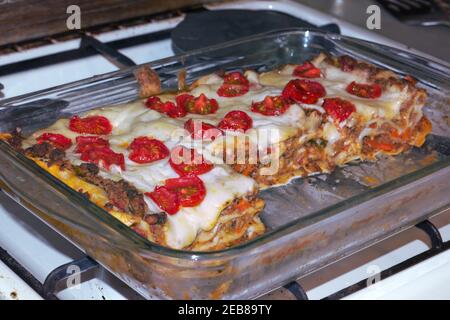 homemade lasagna with cherry tomatoes in glass baking dish, on stovetop grate Stock Photo