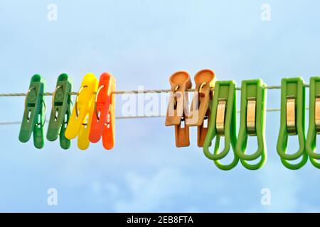 different laundry clothespins of color plastic, with metal clamping (ring as spring). hanging on a clothesline twine outdoors (against an overcast sky Stock Photo
