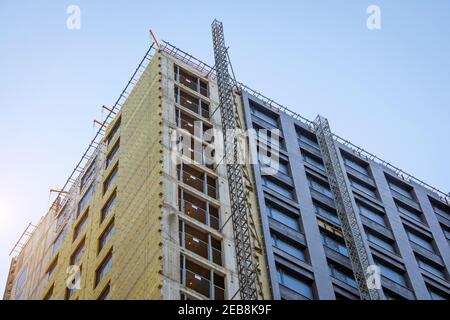Corner of a multi-storey building under construction and a construction elevator rail outside the building to lift workers Stock Photo