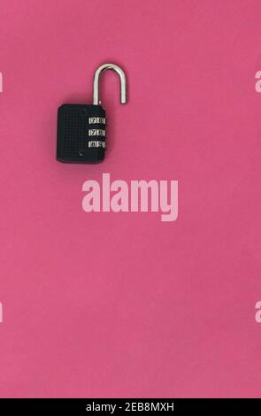 detail of a black padlock with a combination of open numbers with copy space on pink background concept of security and danger Stock Photo