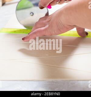Woman's hand cutting pastry for croissants with roller knife. Stock Photo