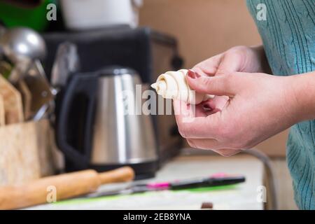 Woman on home kitchen making croissants from puff pastry. Stock Photo