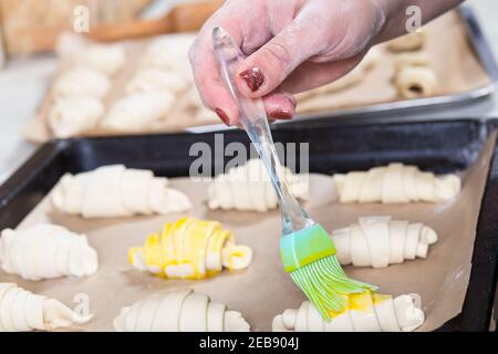 Woman's hand brushing raw croissants on baking paper. Stock Photo