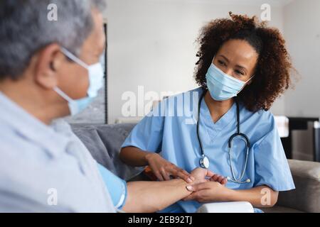 Senior mixed race man with female doctor home visiting wearing face masks taking pulse Stock Photo