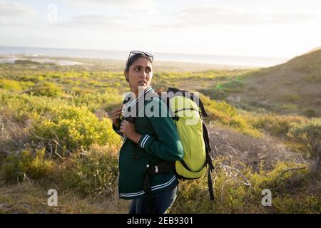 Mixed race woman wearing a backpack and hiking in mountains by the coast Stock Photo