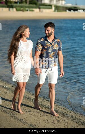Young couple walking together on the beach. They are holding hands and smiling . Stock Photo