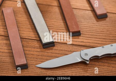 Close-up on a folding knife and various whetstones on wooden background Stock Photo