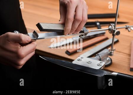 Close-up on hands inserting a whetstone into a manual sharpener machine Stock Photo