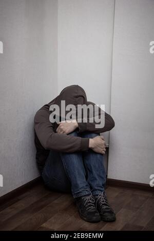 desperate young drug addict wearing hood and sitting alone in corner. concept of sadness, depressed and life problems Stock Photo