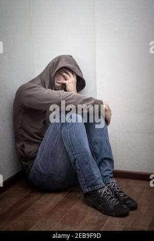 desperate young drug addict wearing hood and sitting alone in corner. concept of sadness, depressed and life problems Stock Photo