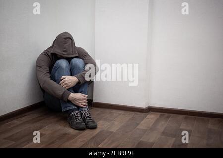 desperate young drug addict wearing hood and sitting alone in corner. concept of sadness, depressed and life problems Stock Photo