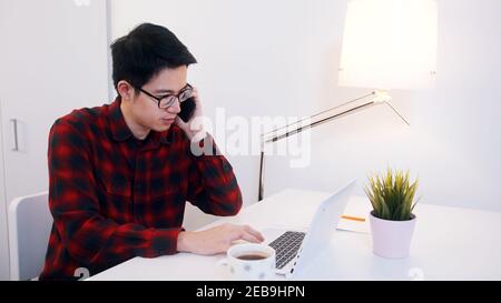 Young asian man speaking on the phone while workingo n laptop in the office. High quality photo Stock Photo
