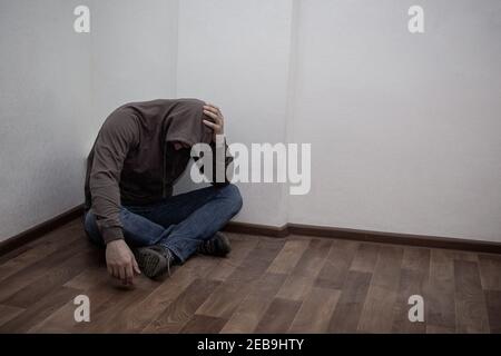 desperate young drug addict wearing hood and sitting alone in corner. concept of sadness, depressed and life problems Stock Photo