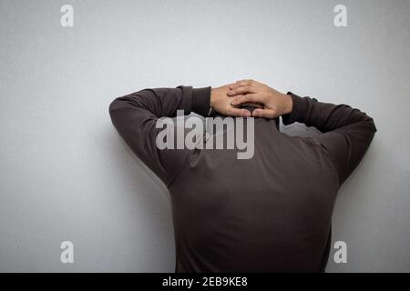 Criminal in grey hoodie with hands behind head being arrested near white wall with copy space Stock Photo