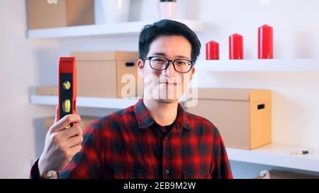 Young asian handyman holding leveler indoors. High quality photo Stock Photo